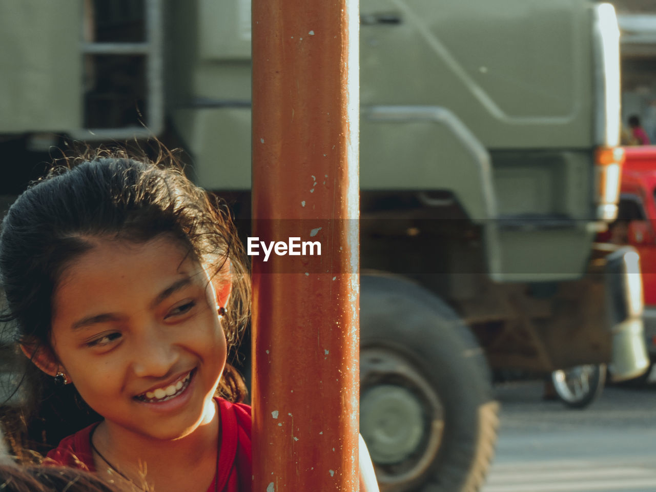 Close-up of smiling girl looking away by pole