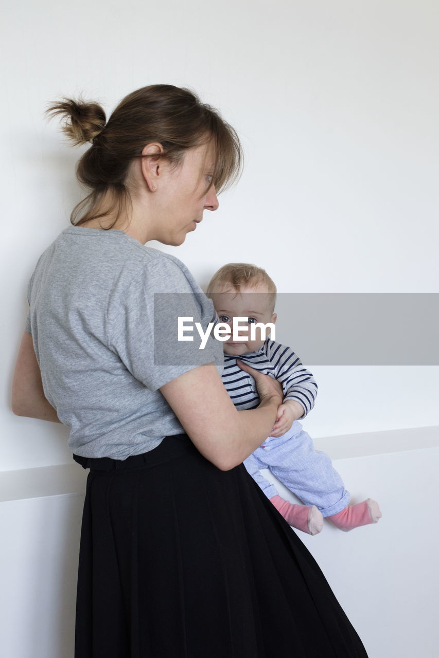 Woman carrying son while standing against wall