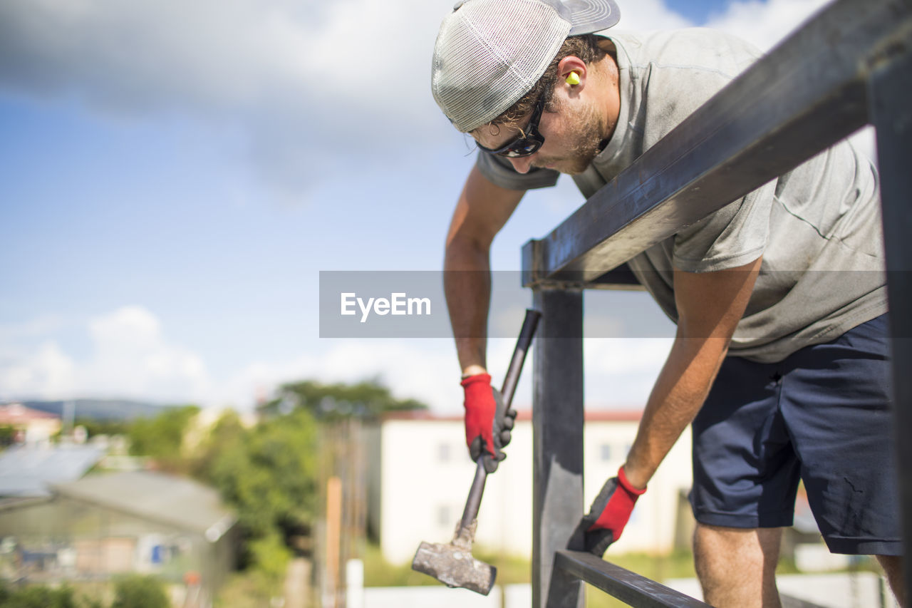 Construction worker using hammer to build steel railing on roof.