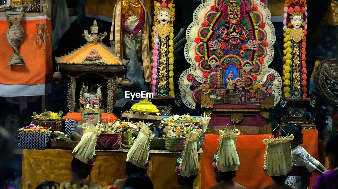 Women wearing traditional hats sitting in front of religious statues at temple