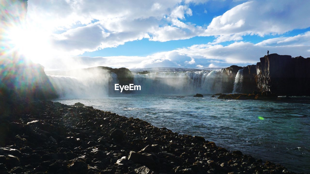 Scenic view of waterfall against cloudy sky