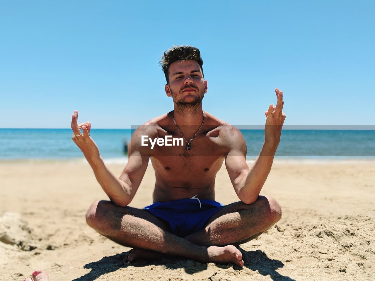 Full length of shirtless man doing yoga at beach against sky