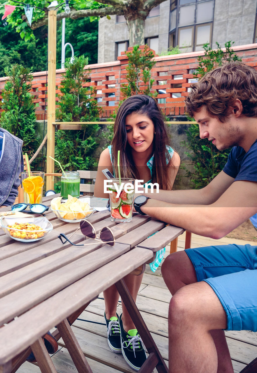 Friends using mobile phone by food and drink at restaurant