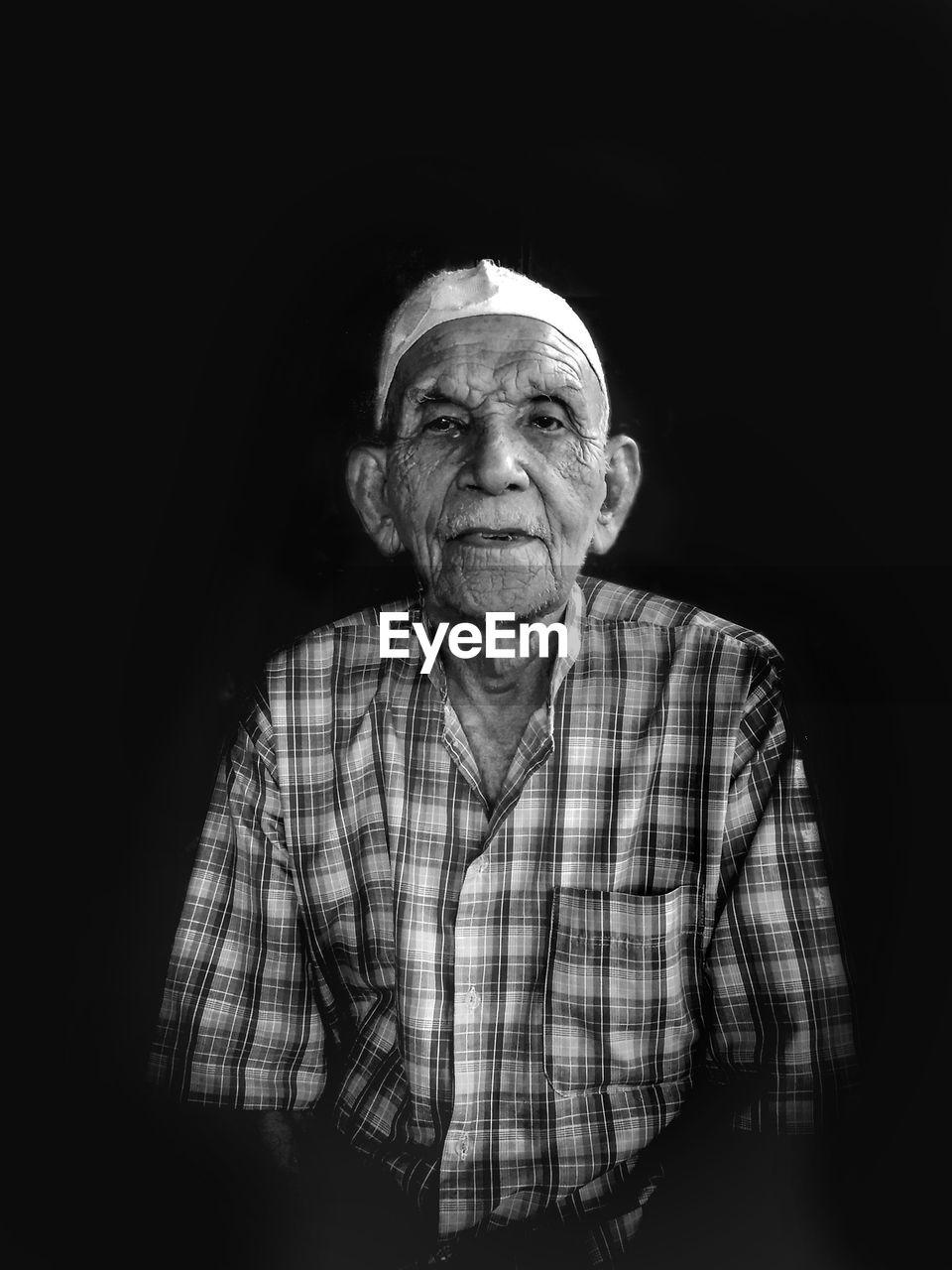 Portrait of senior man in skull cap sitting against black background