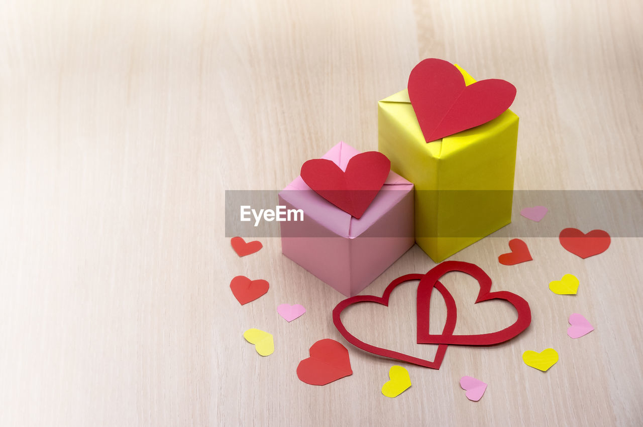 heart, heart shape, love, positive emotion, emotion, font, pink, indoors, no people, wood, still life, red, multi colored, paper, valentine's day, studio shot, copy space, petal, creativity, high angle view, yellow, ribbon, table, gift, shape, close-up