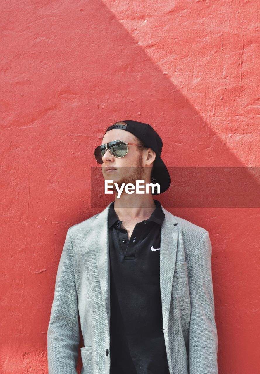 Young man wearing sunglasses while standing against wall