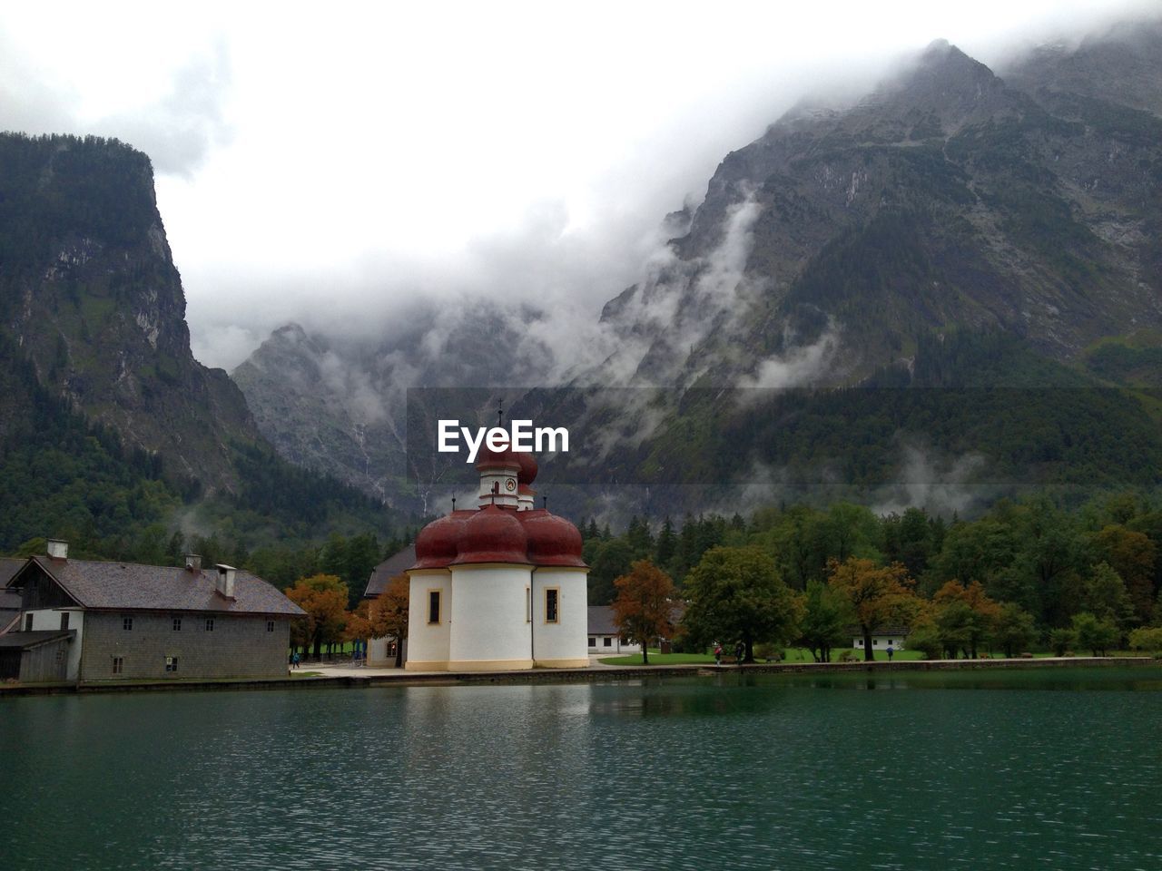 House and church at lakeshore against rocky mountains