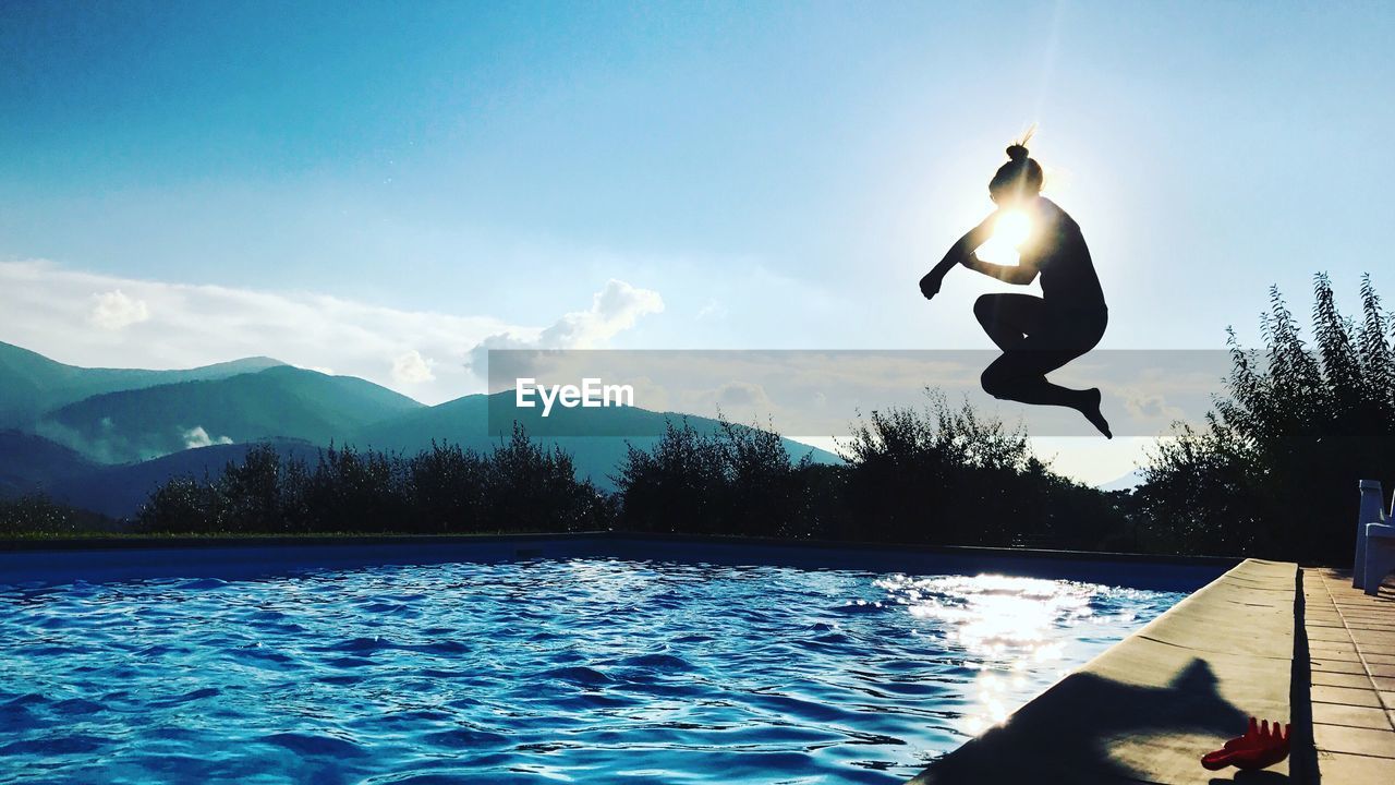 Silhouette woman jumping in swimming pool against sky