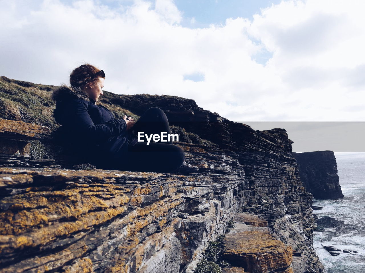 Full length of woman sitting on rock against cloudy sky