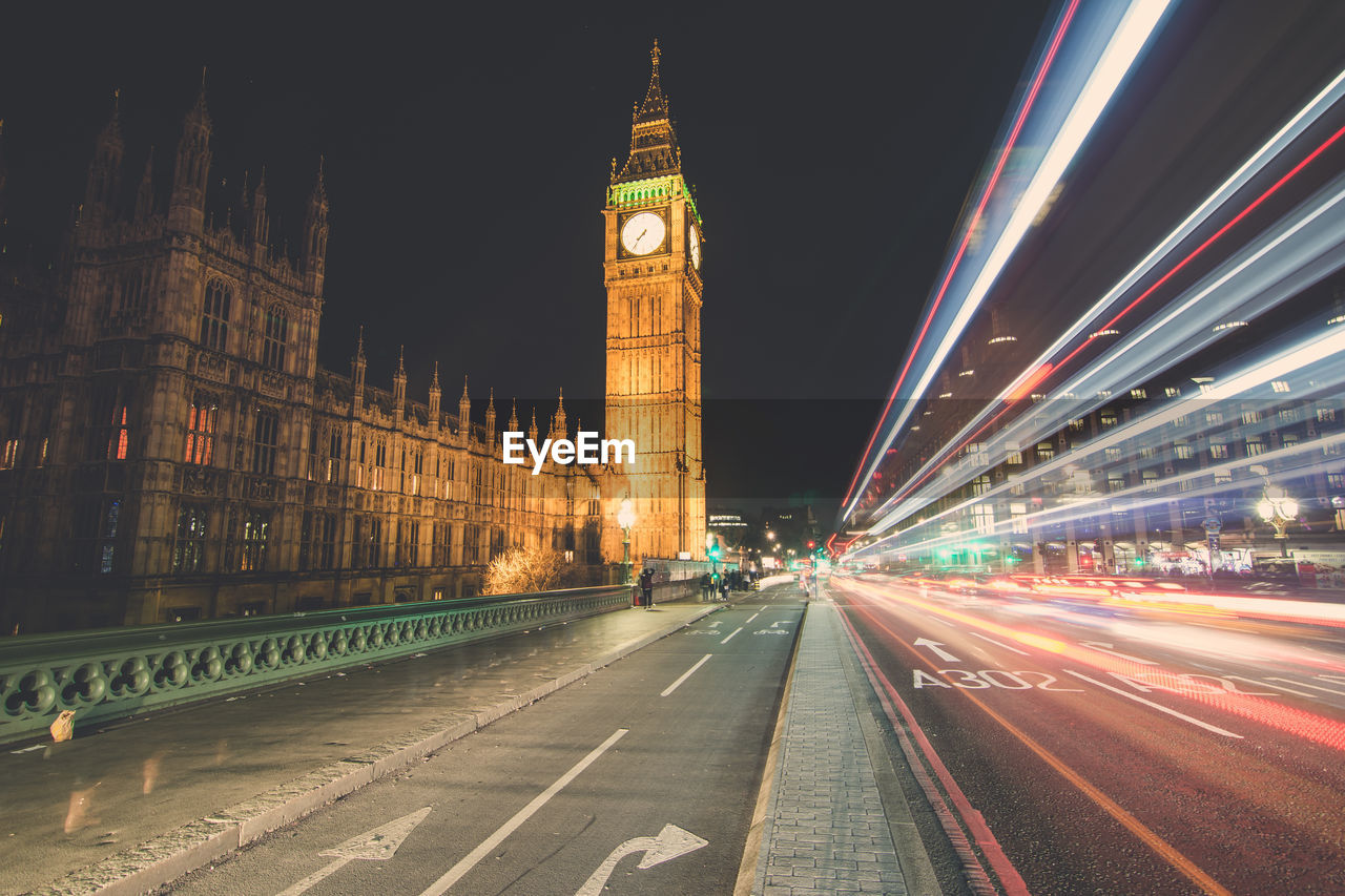 Light trails on road by big ben against sky