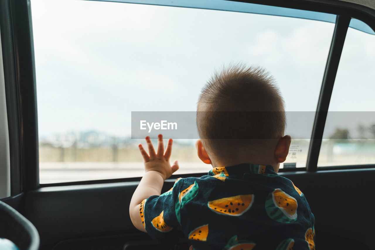 Rear view of boy looking through car window