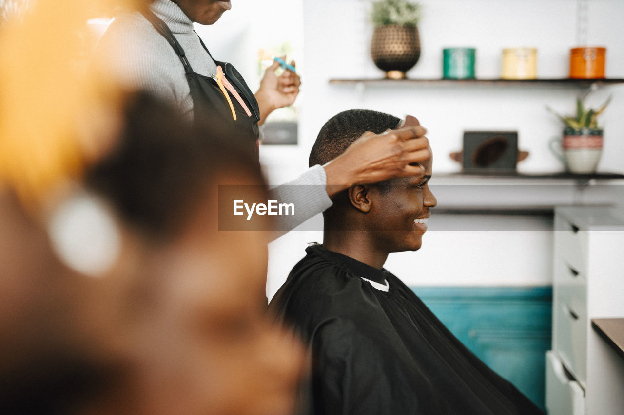 Midsection of female hairdresser cutting hair of smiling male customer in barber shop