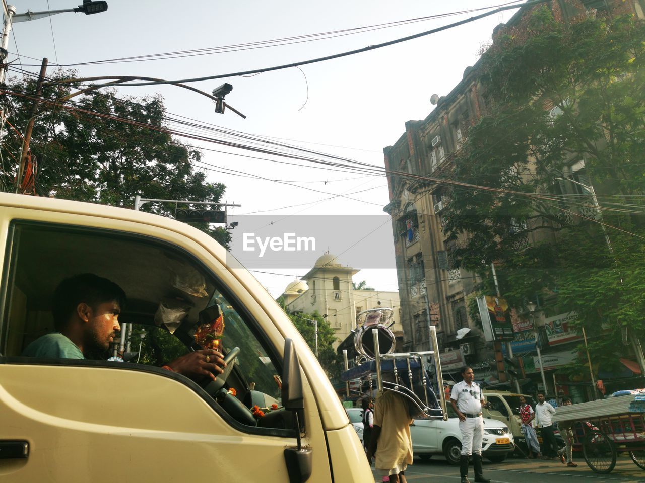 mode of transportation, transportation, car, motor vehicle, city, architecture, street, men, land vehicle, adult, transport, travel, vehicle, group of people, cable, road, day, city life, nature, tree, on the move, rickshaw, women, lifestyles, city street, public transport, sky, building exterior, plant, outdoors, motion, built structure, taxi, driving, public transportation, electricity, traffic, leisure activity, person