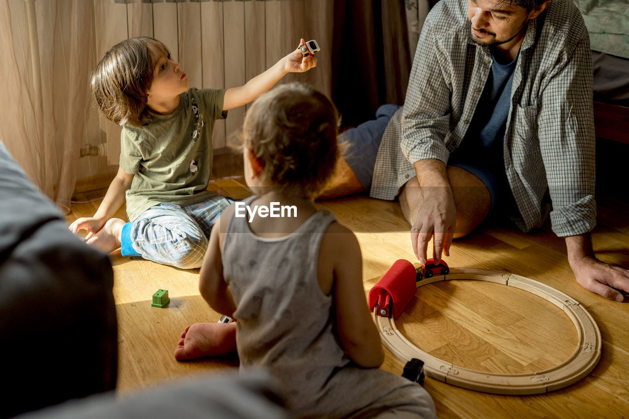 Father and sons spending leisure time playing with toys at home