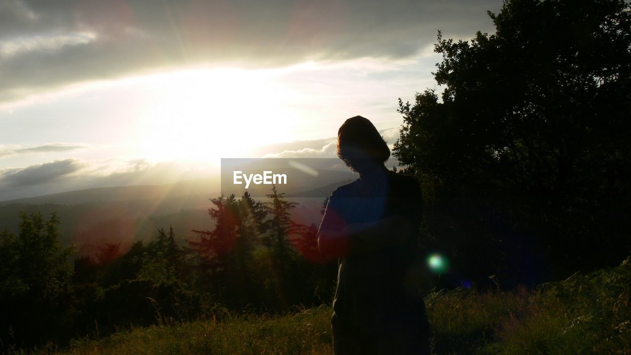 Woman standing by trees against sky during sunset