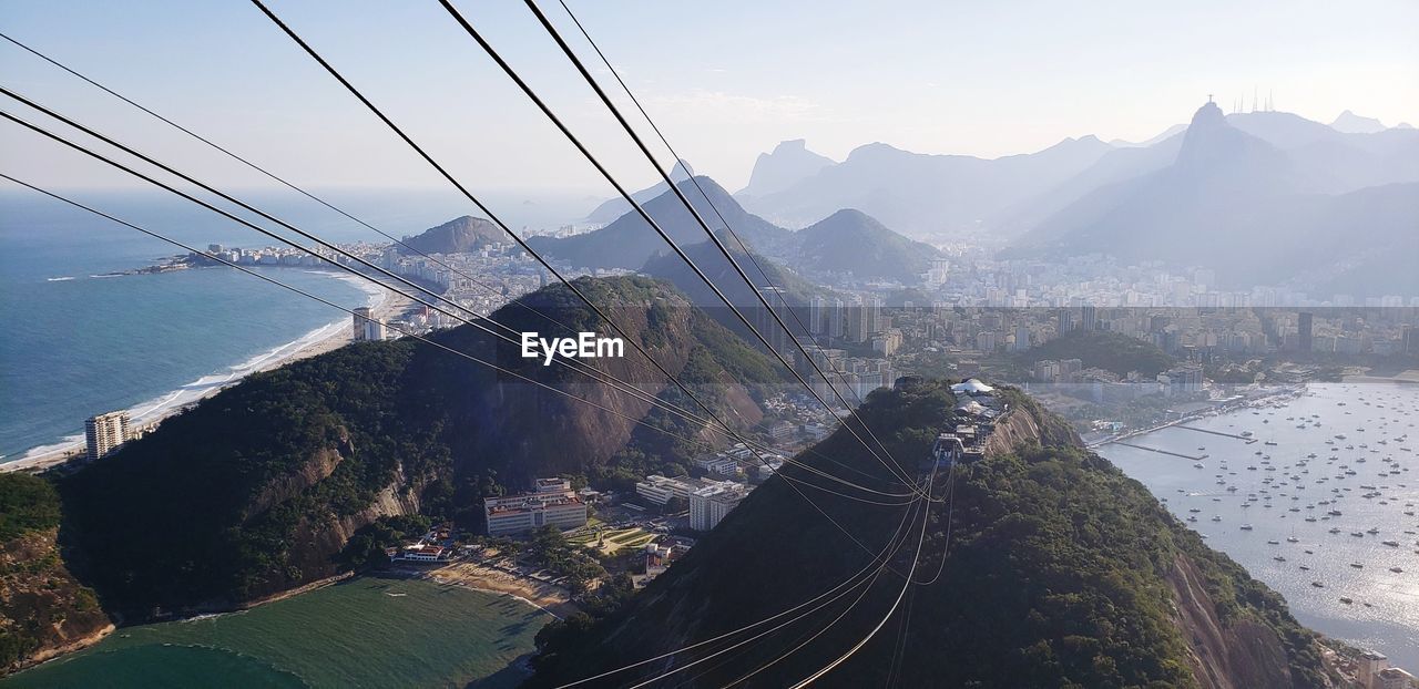 Overhead cable car over sea and mountains against sky