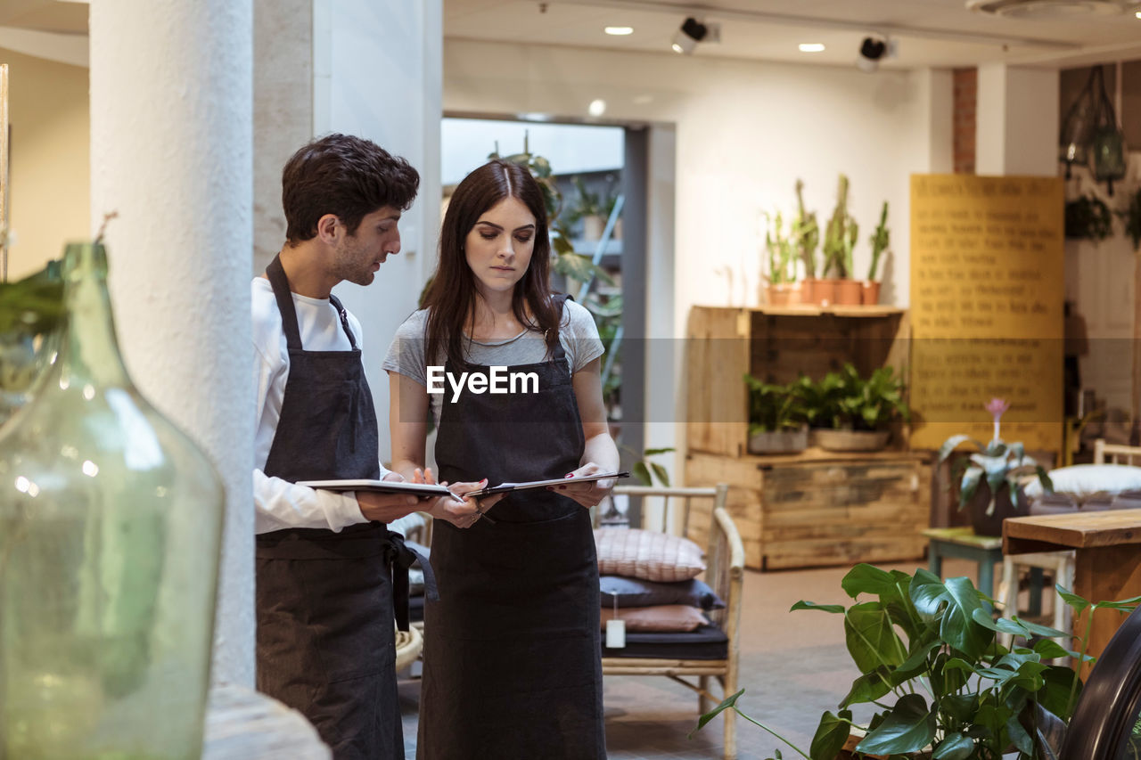 Male and female colleague discussing over digital tablet while standing in boutique