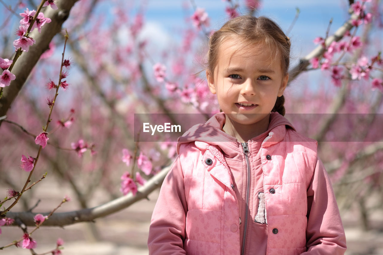 Portrait of cute girl standing against cherry trees