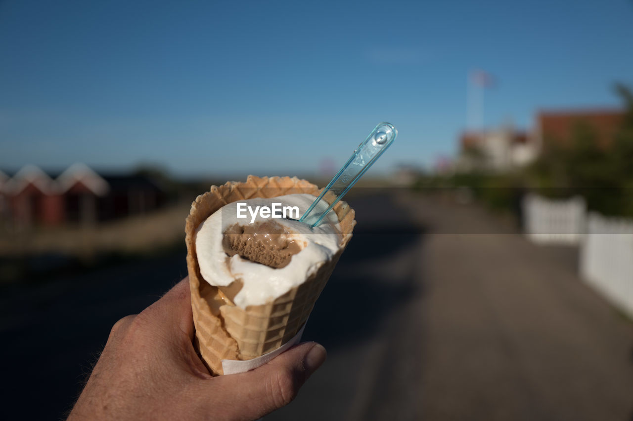 Close-up of hand holding ice cream cone against sky