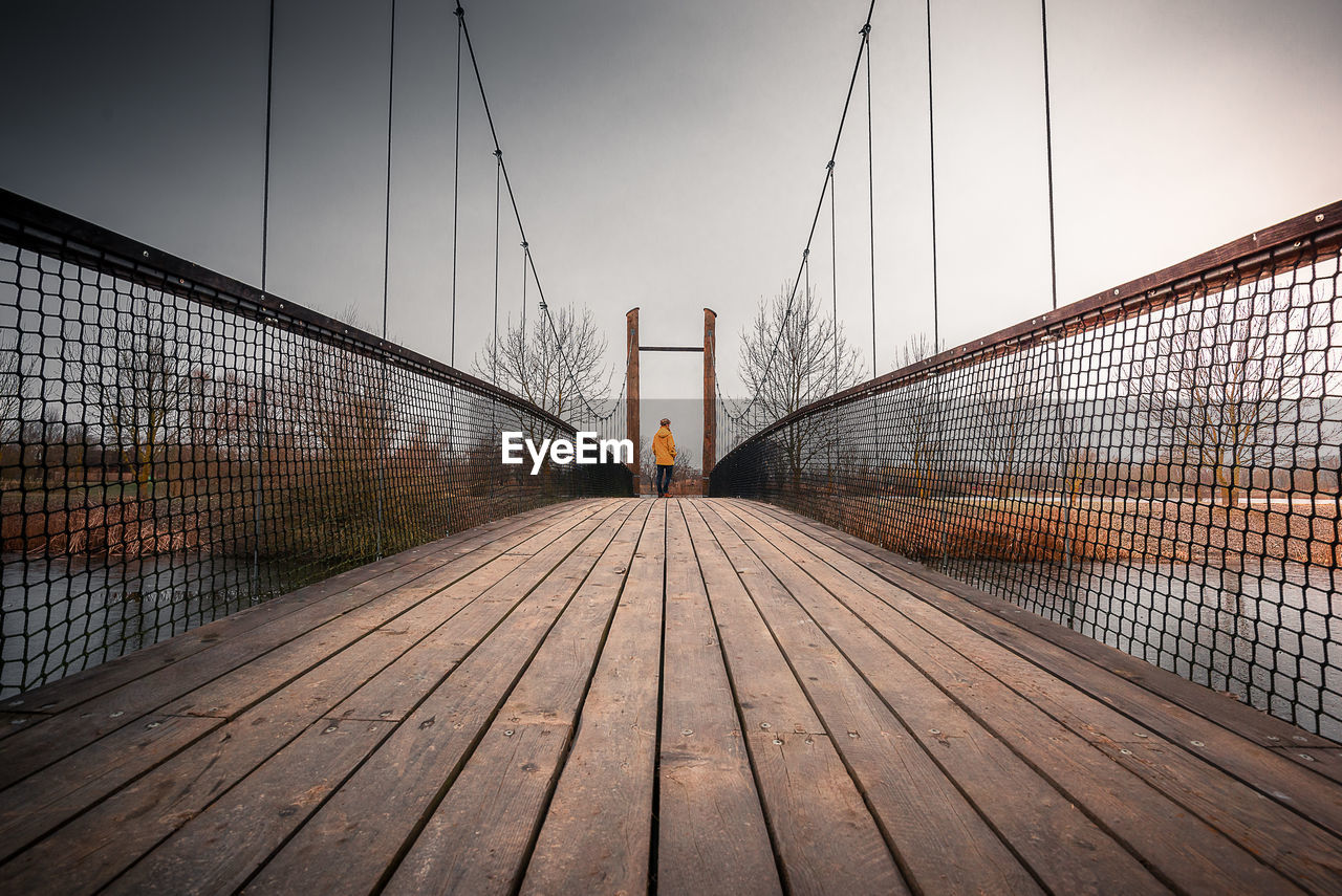 Rear view of woman on footbridge against sky