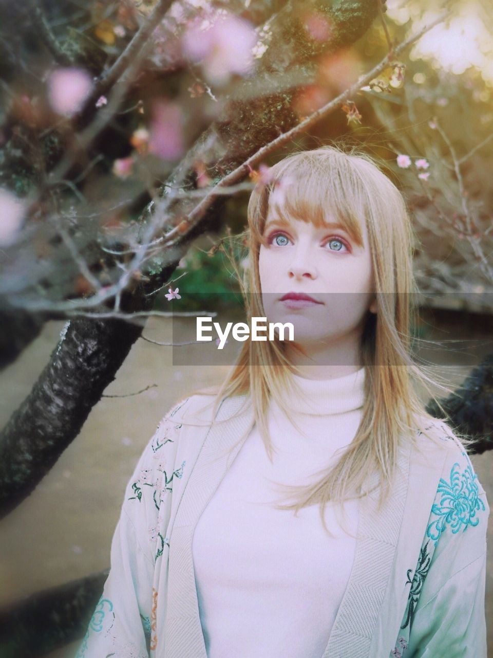 Beautiful young woman looking away standing by tree