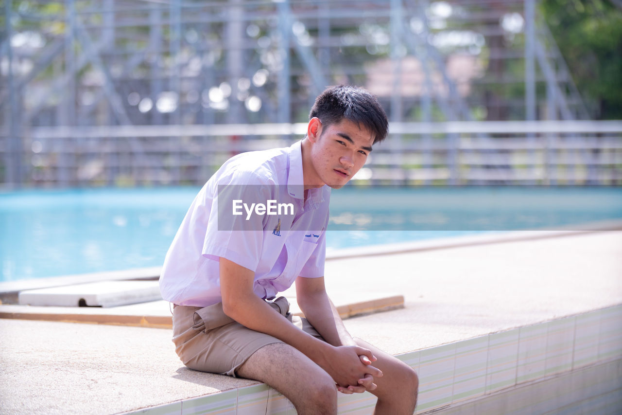 YOUNG MAN SITTING AT SWIMMING POOL