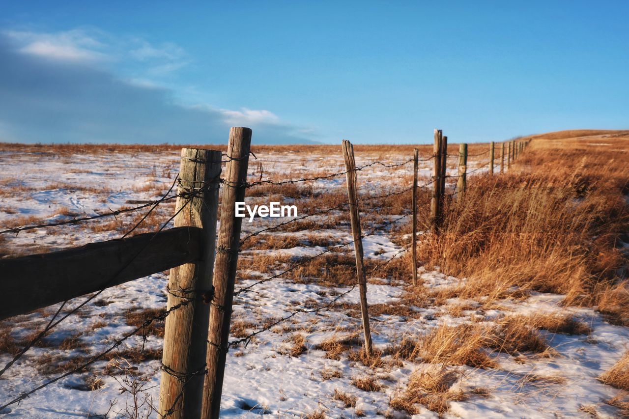 Wooden fence on snow covered field against sky