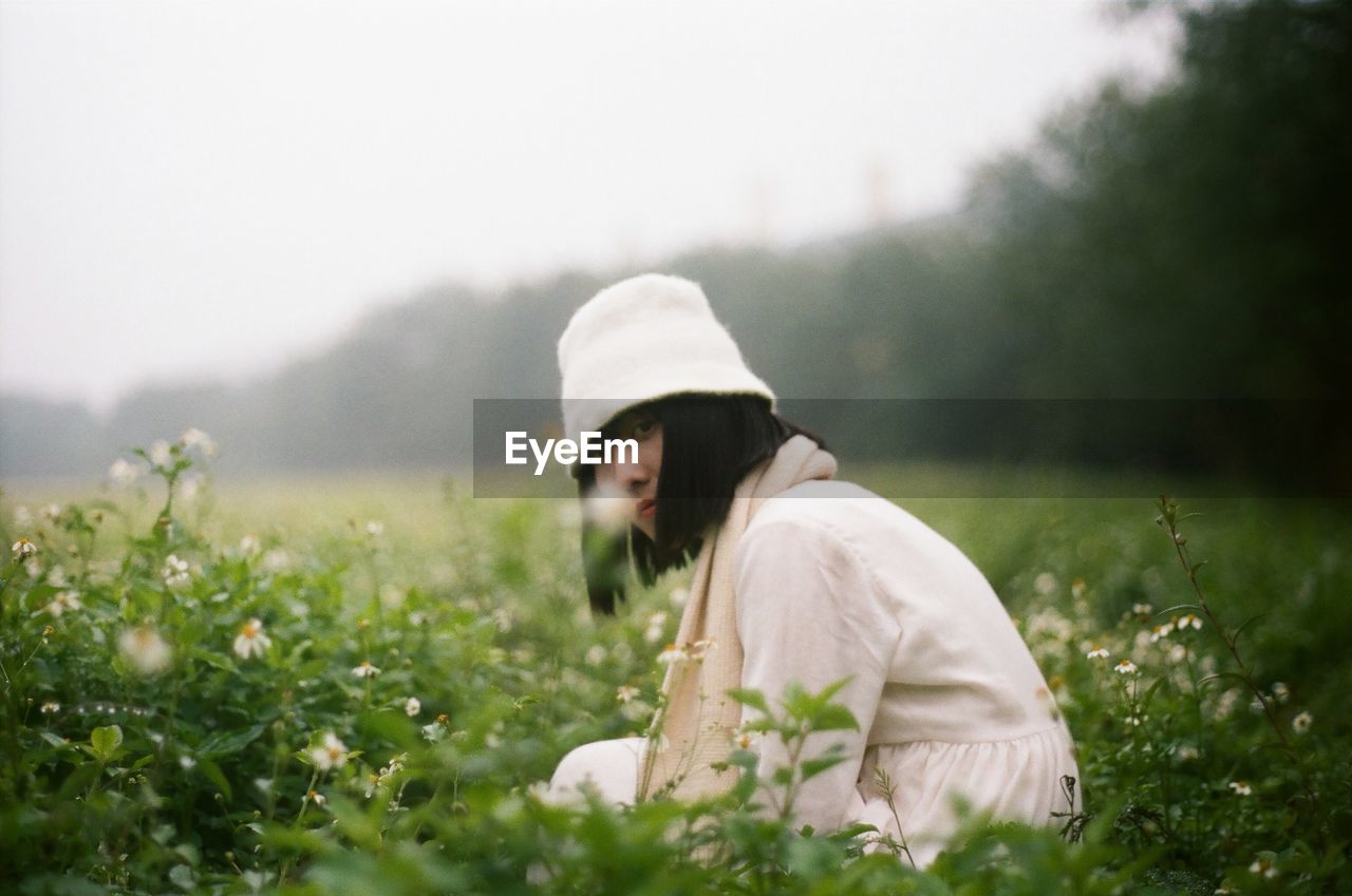 Serious woman crouching on green meadow