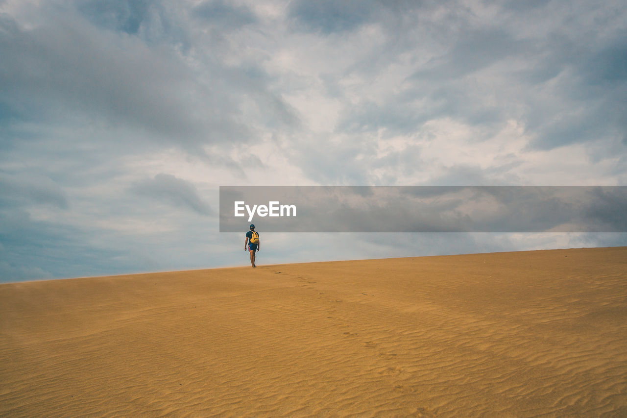 Rear view of man with backpack walking on sand dune in desert