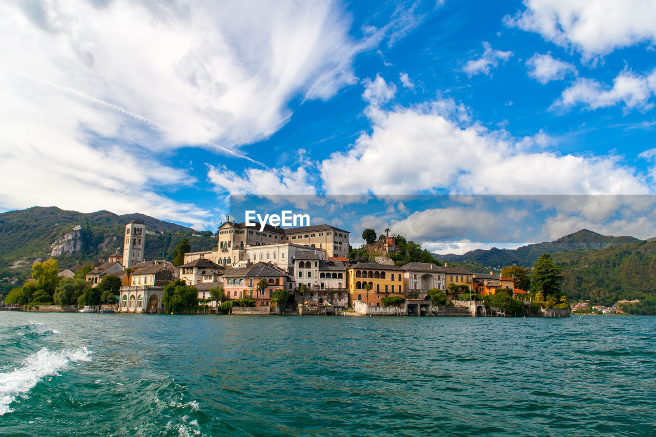 Isola san giulio inside orta's lake, piemonte, italy, from water surface with blue sky.