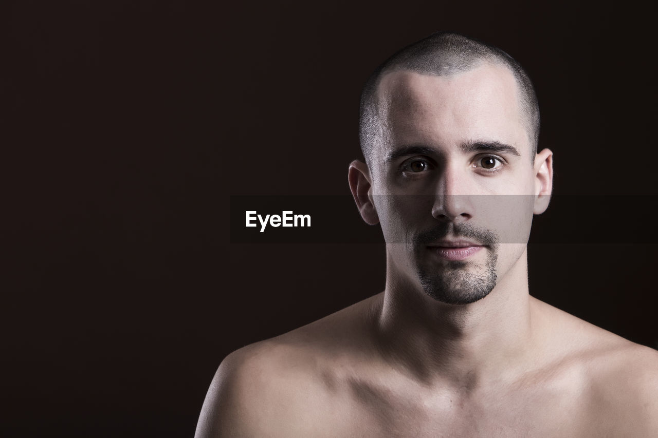 Portrait of handsome shirtless man against black background