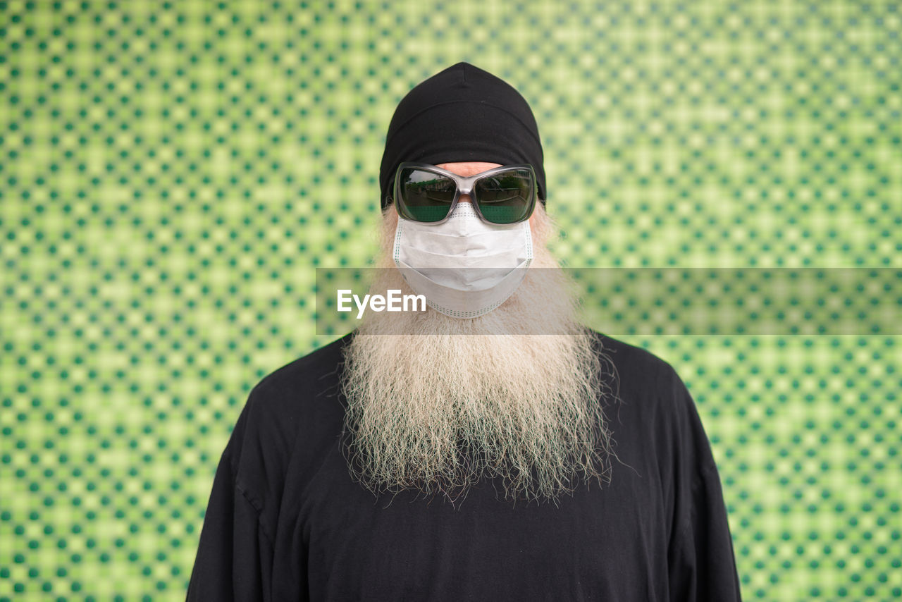 Portrait of man wearing sunglasses standing against green background