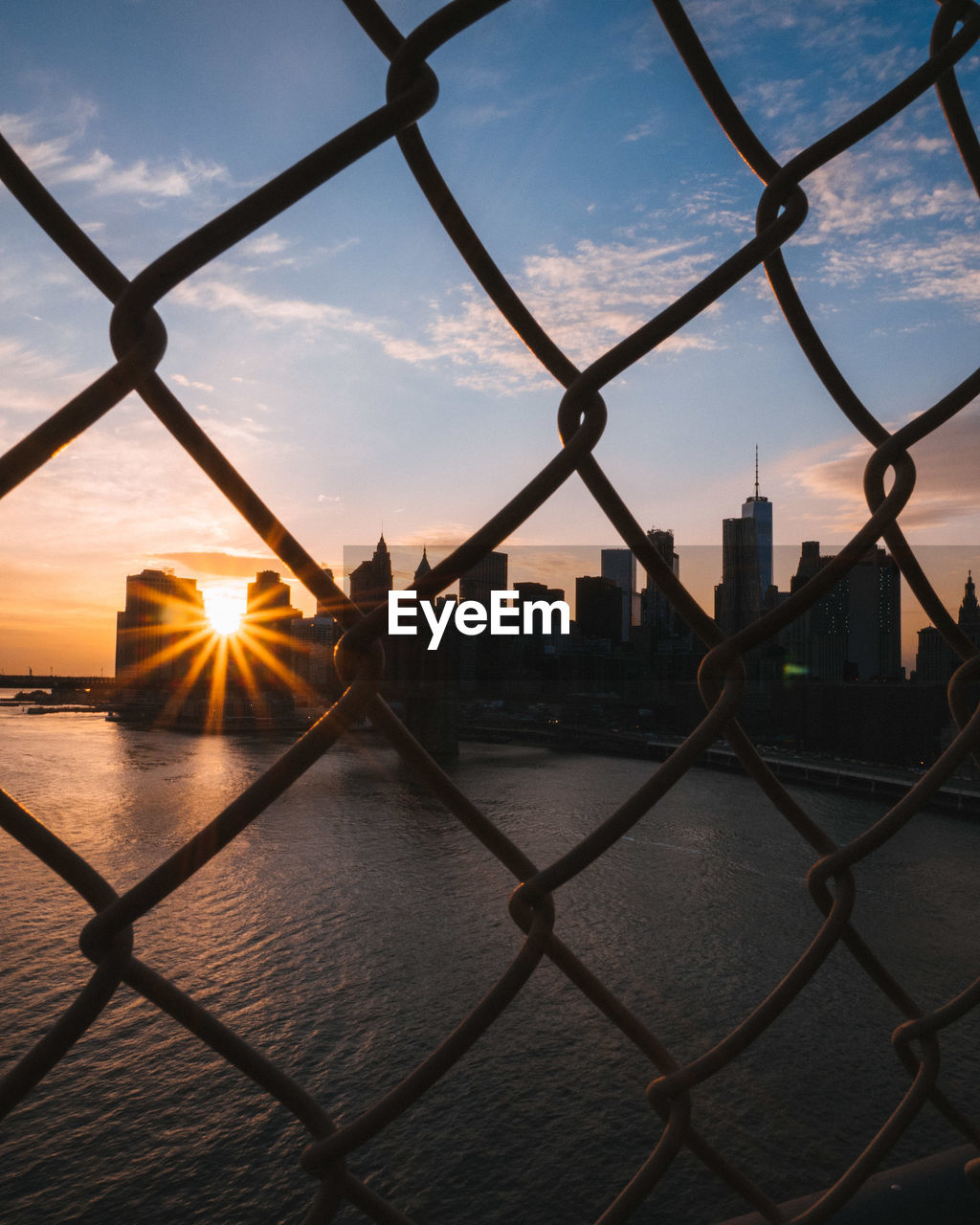 Cityscape by river seen through chainlink fence