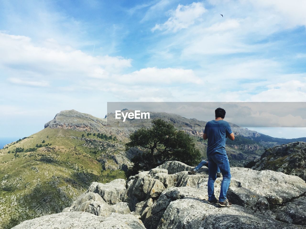 Rear view of man standing on rock at serra de tramuntana against cloudy sky