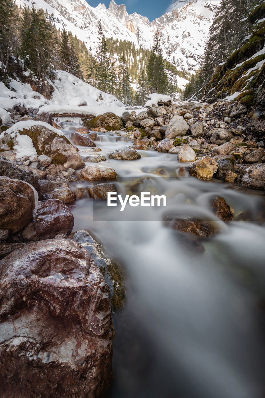 STREAM FLOWING THROUGH ROCKS AGAINST MOUNTAIN