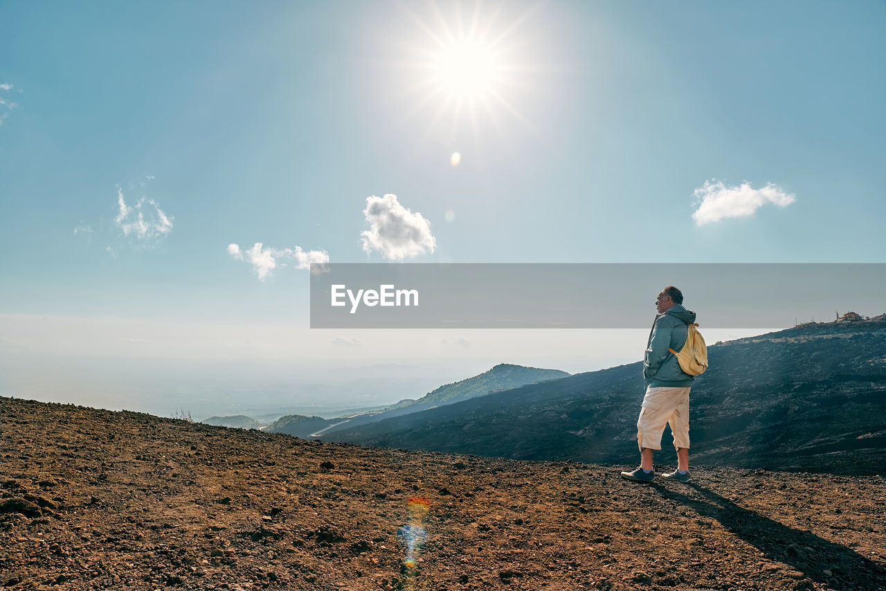 Rear view of man looking through binoculars at panoramic view of summits volcano etna