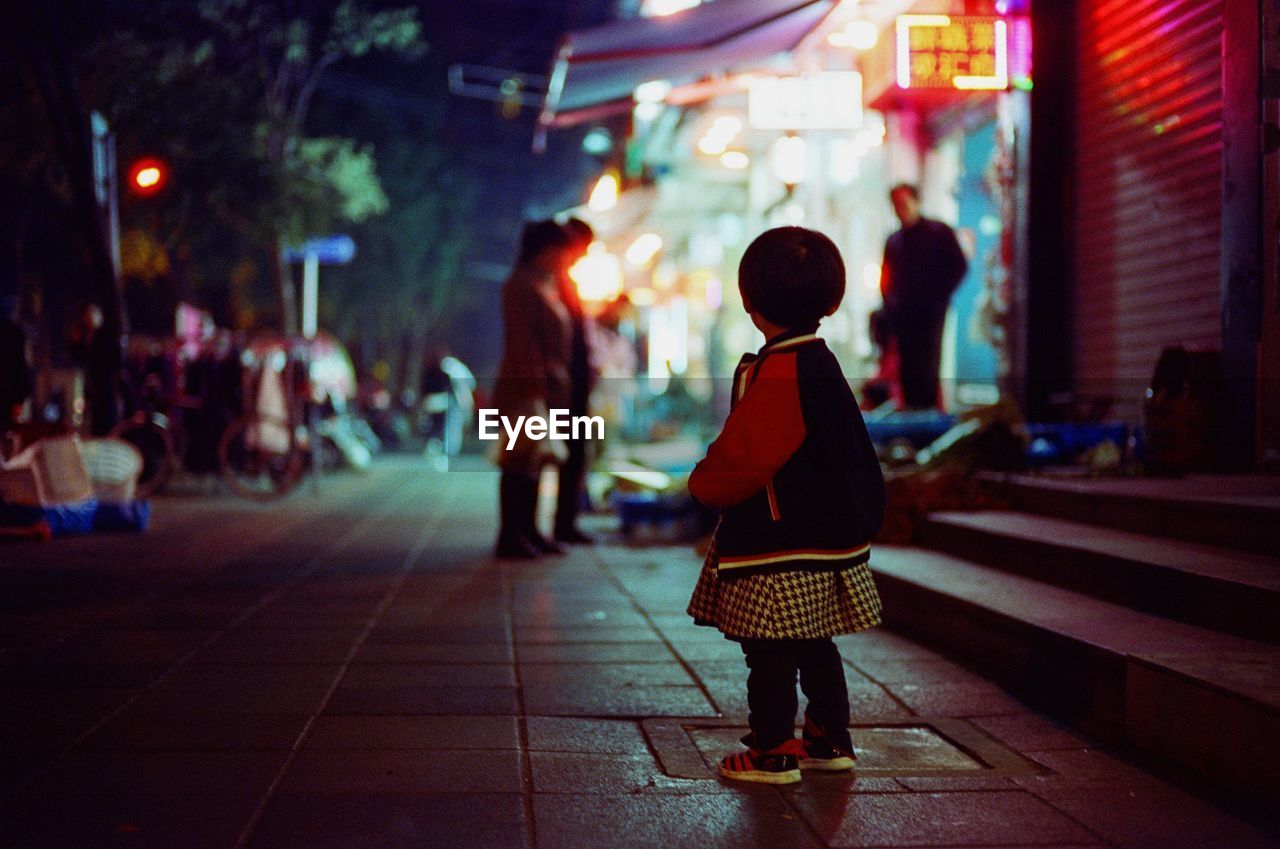 Rear view of girl standing on footpath at night