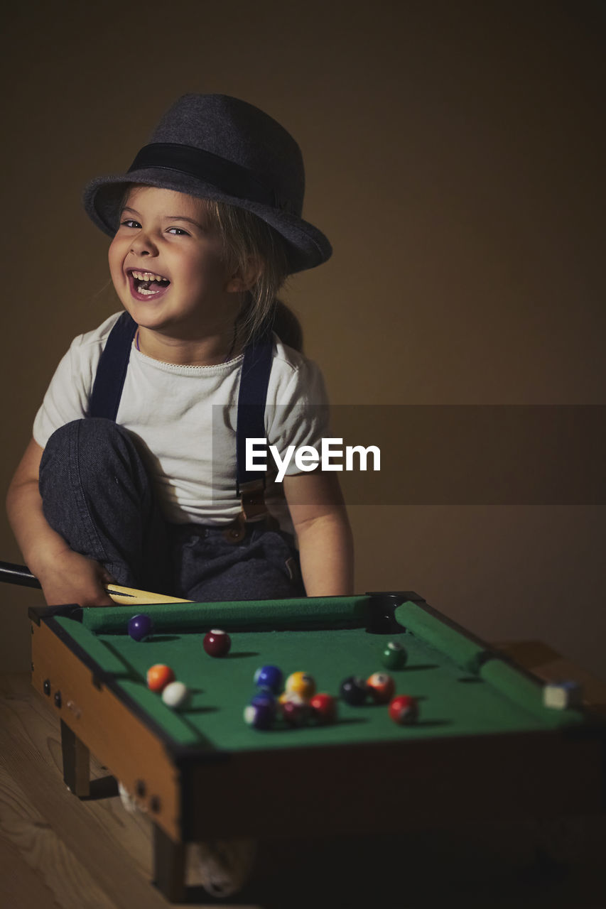 Charming child in retro clothes playing toy billiards.