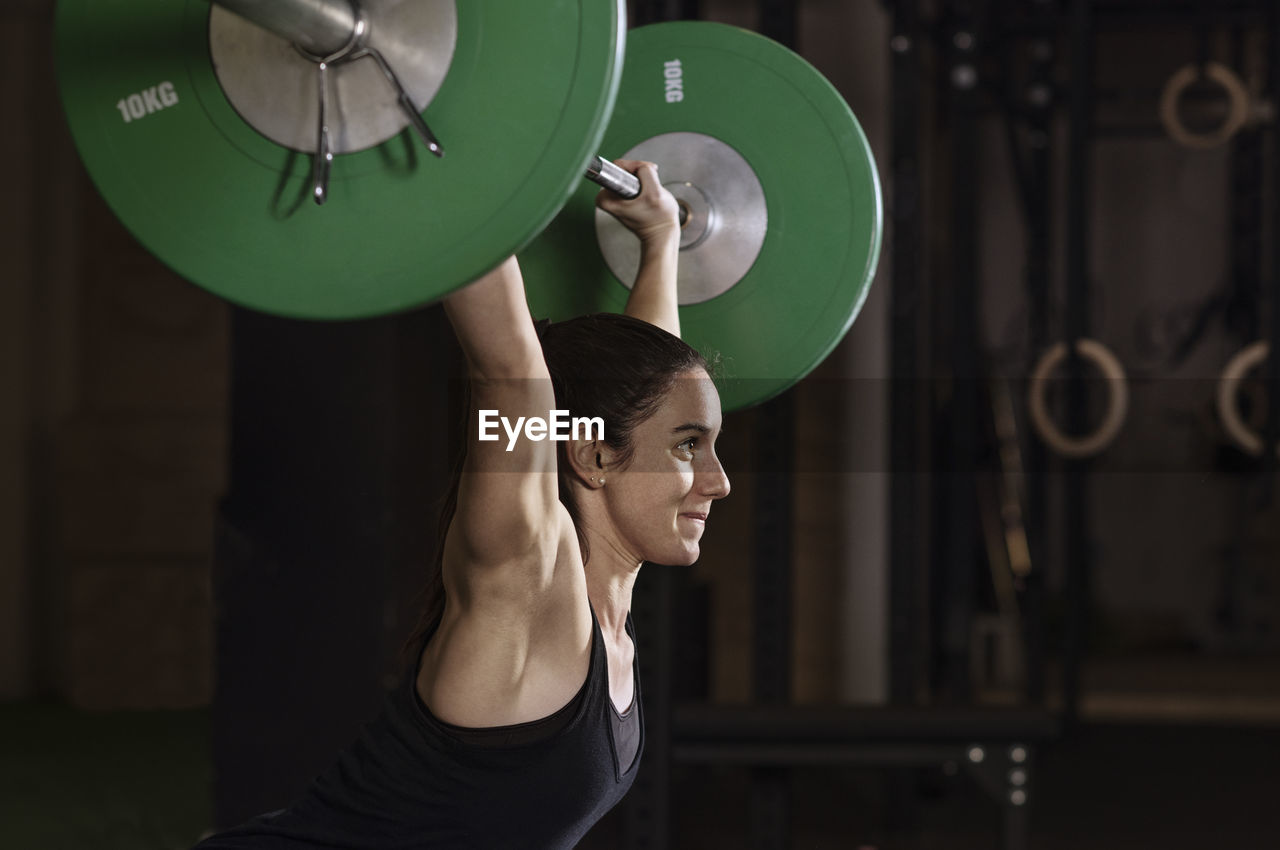 Side view of determined female athlete lifting barbell in health club