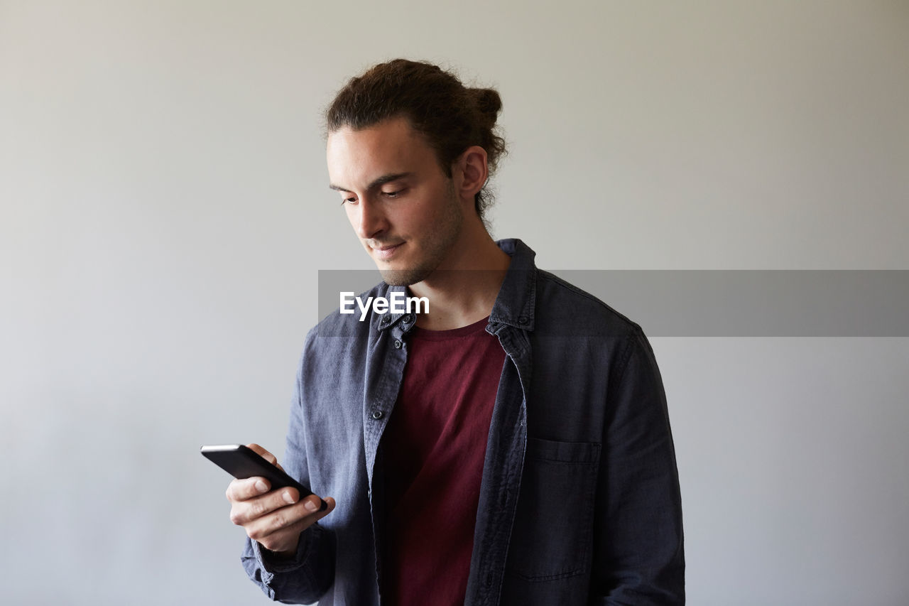 Creative businessman using smart phone against gray wall in office