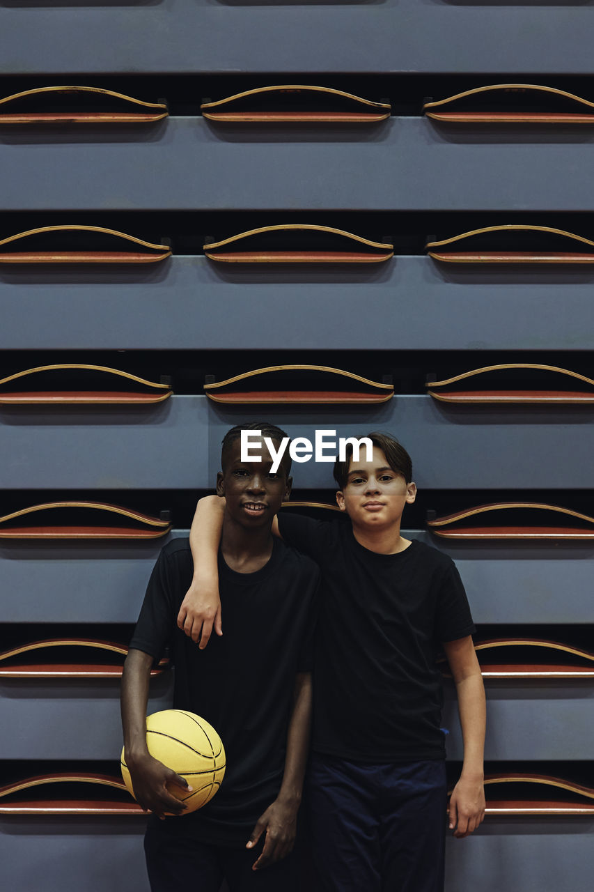 Portrait of teenage boy standing with arm around male friend at sports court