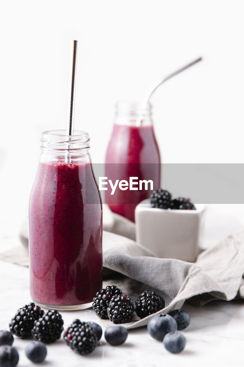 Berries smoothie in glass bottles with reusable metal straws. front vertical shot.