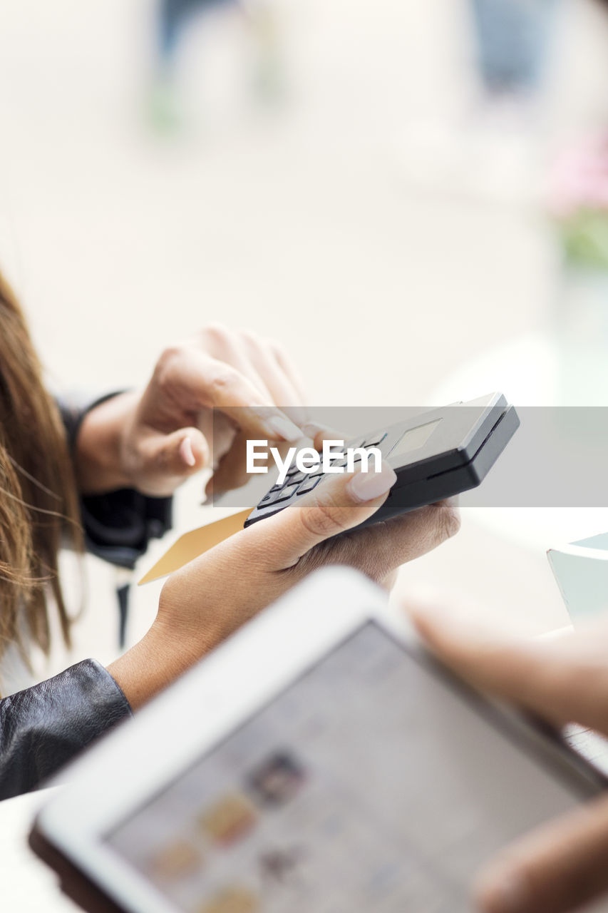 Female customer paying through card reader while owner using digital tablet in food truck