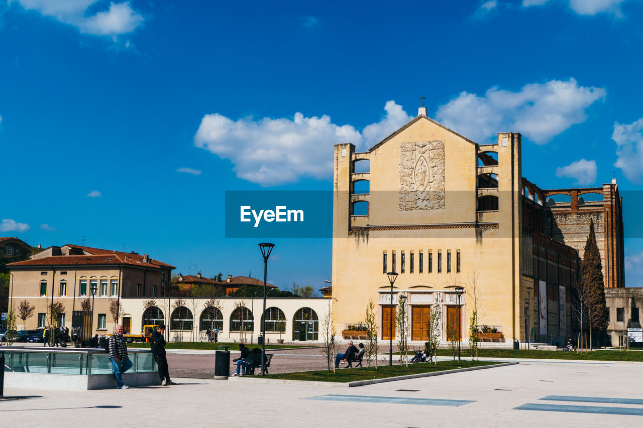 Low angle view of buildings in front of walkway against cloudy blue sky on sunny day