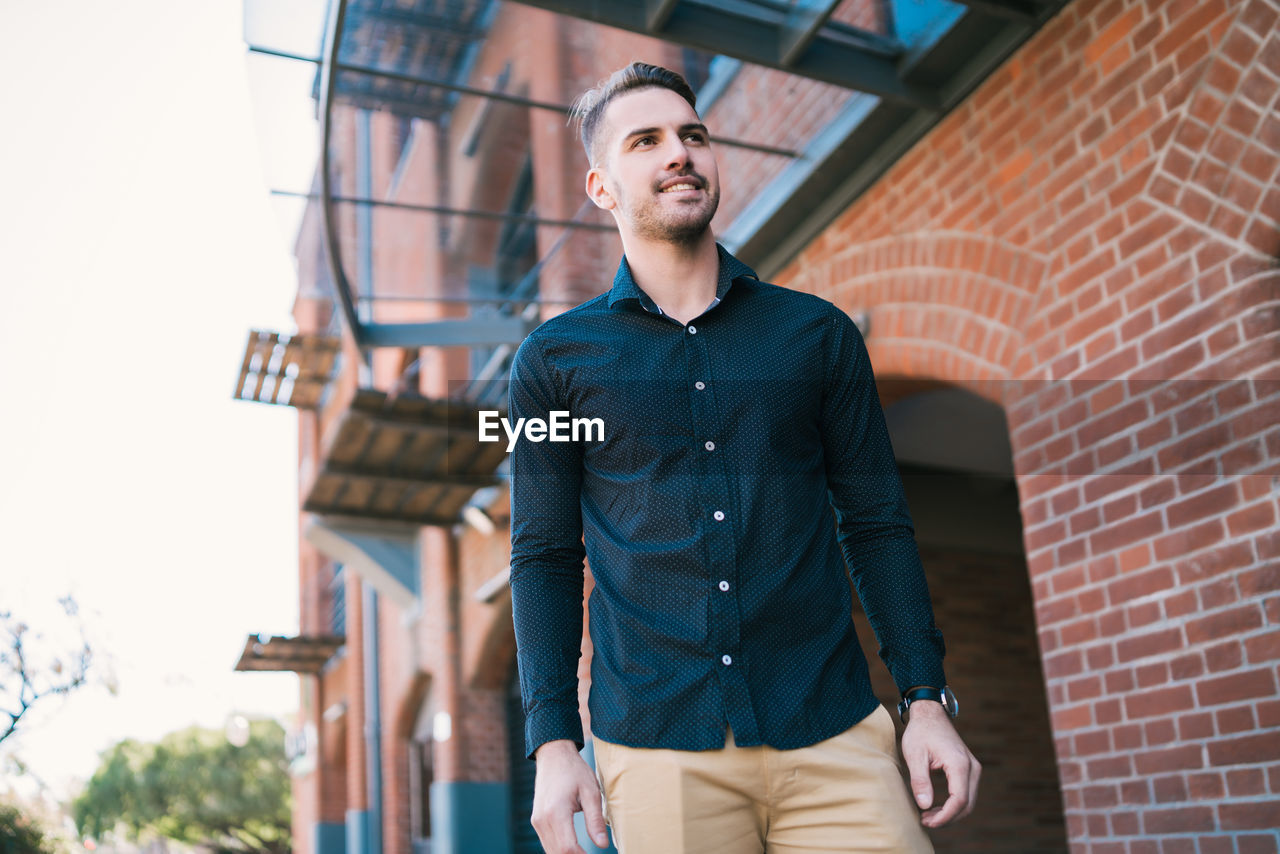 Low angle view of young man looking away standing against building
