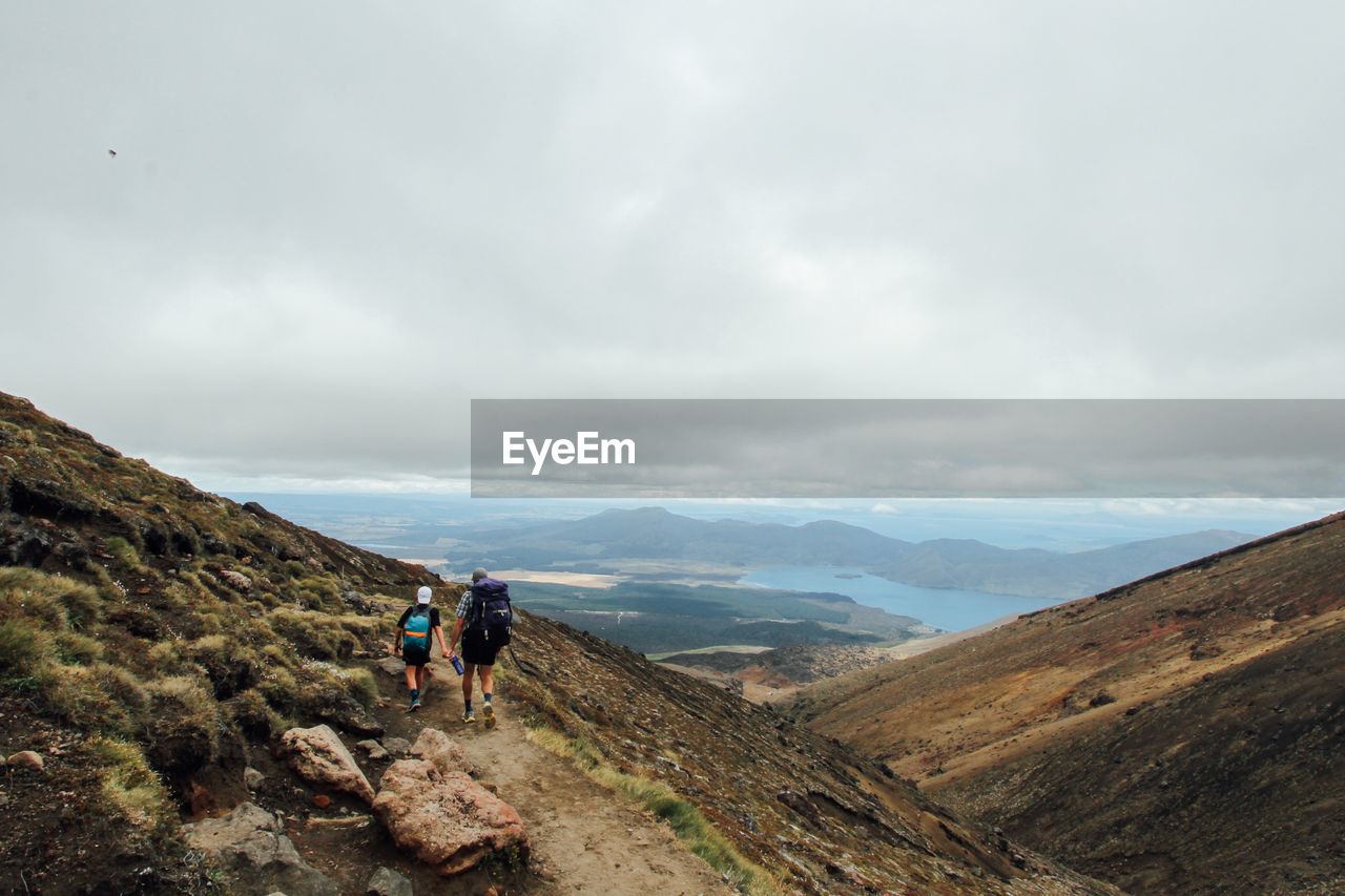 Rear view of man with son hiking on mountain against cloudy sky