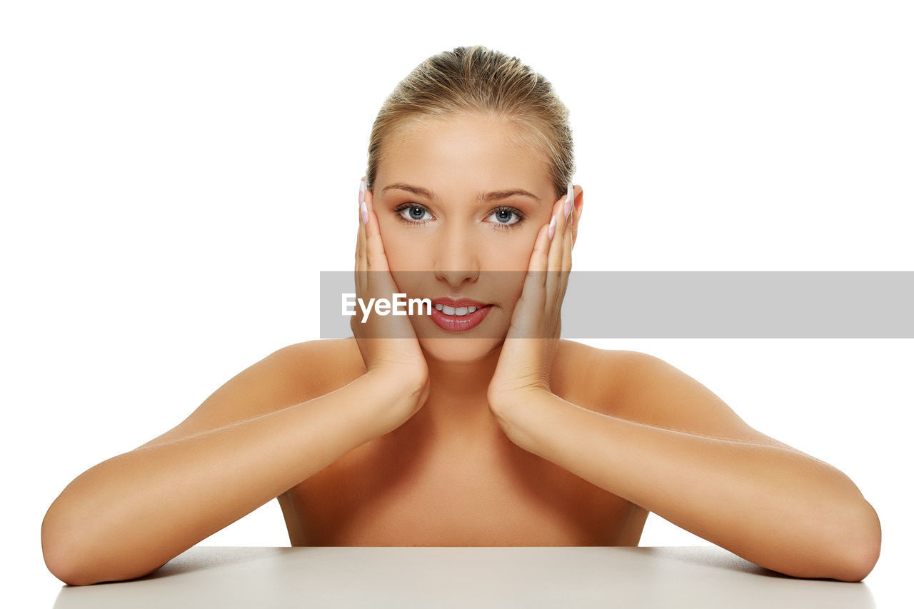 Portrait of young woman with hands on cheeks over table against white background