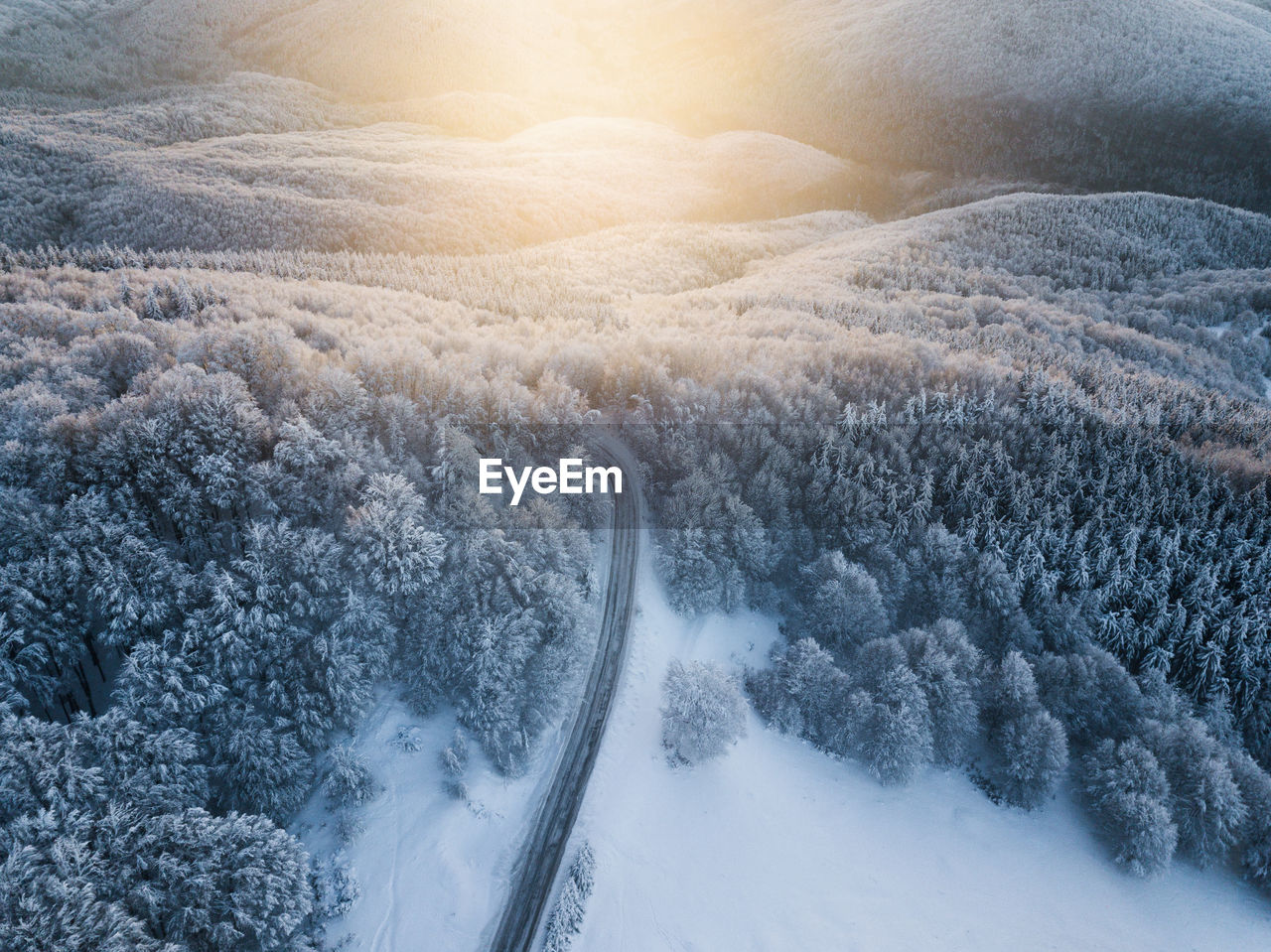 Scenic aerial view of snow covered winter landscape and empty asphalt road at sunrise. 