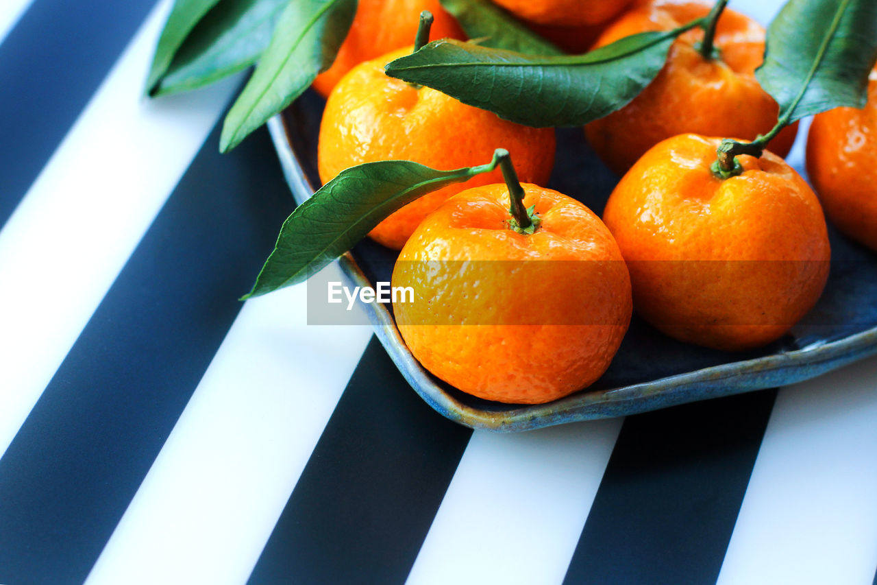 Tangerines with leaves in a blue plate on a black and white background. a symbol of christmas food