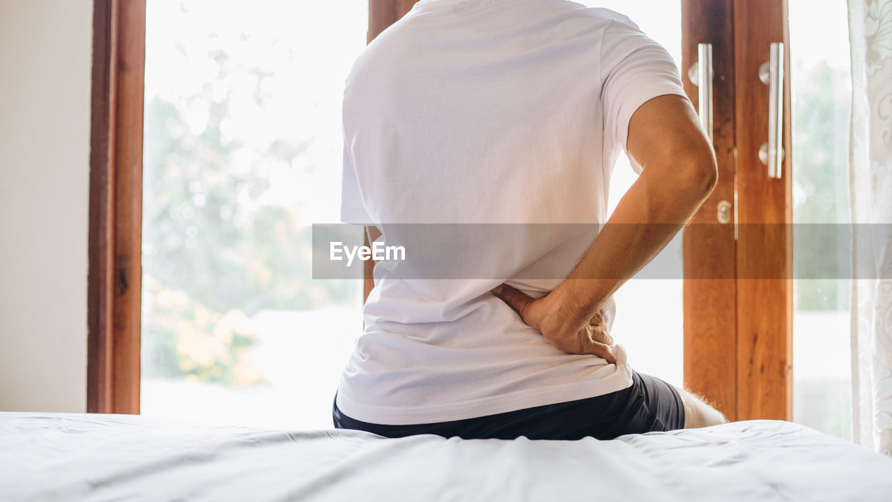 REAR VIEW OF A MAN SITTING ON BED